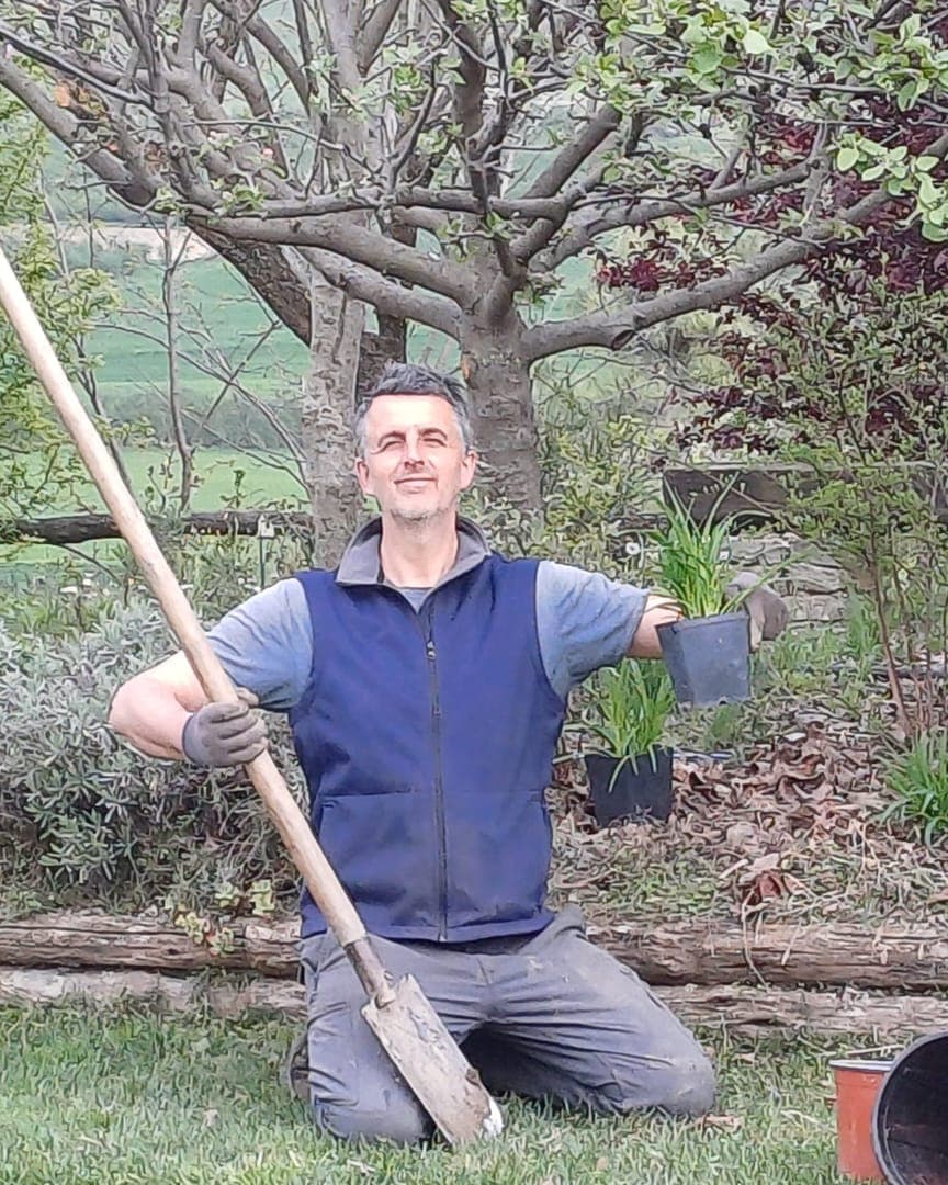 Fulvio Lovisolo in ginocchio in giardino, con la vanga e una pianta in vaso