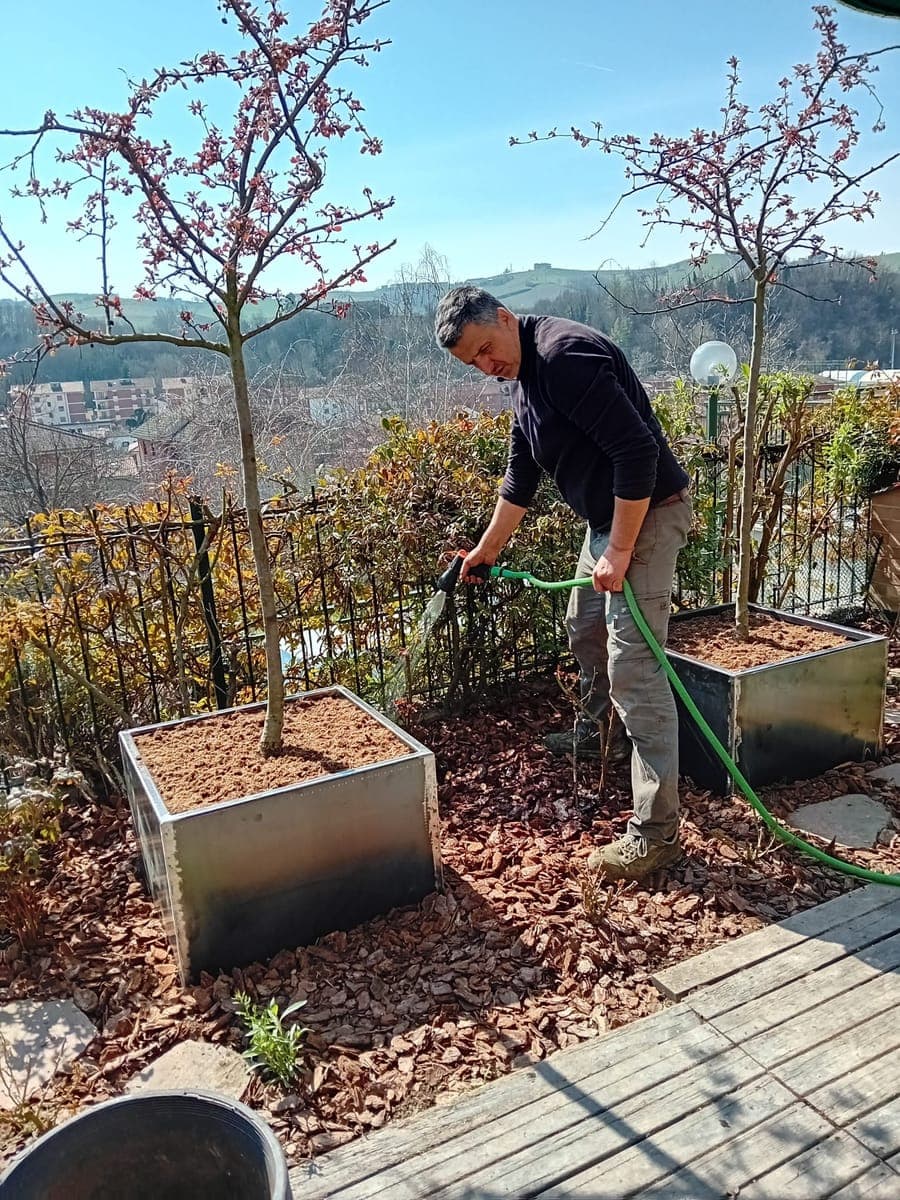 Fulvio Lovisolo annaffia due fioriere in acciaio su una terrazza affacciata sulle colline